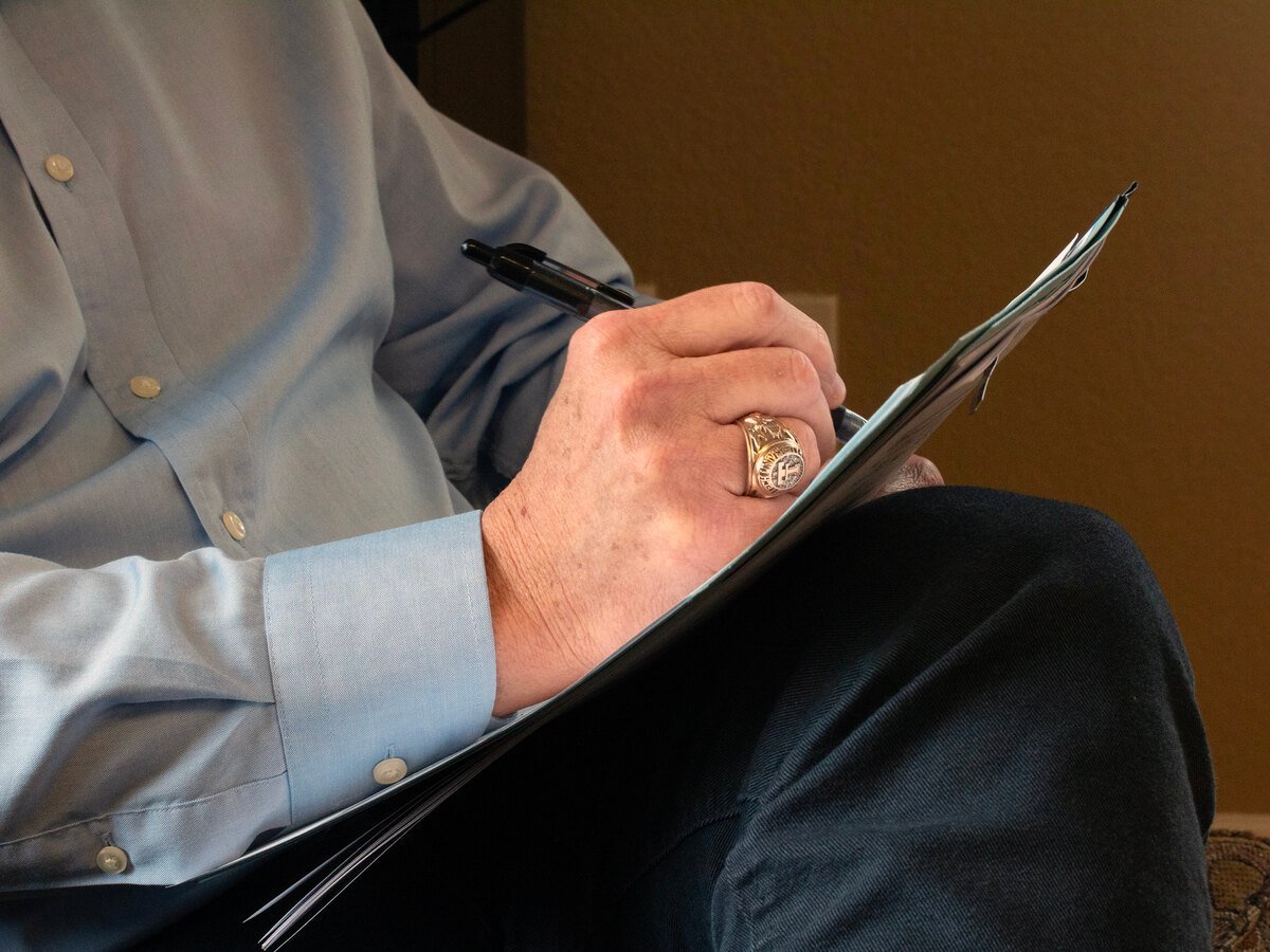 A close-up of hands holding a clipboard and pen, with a decorative ring visible on one hand